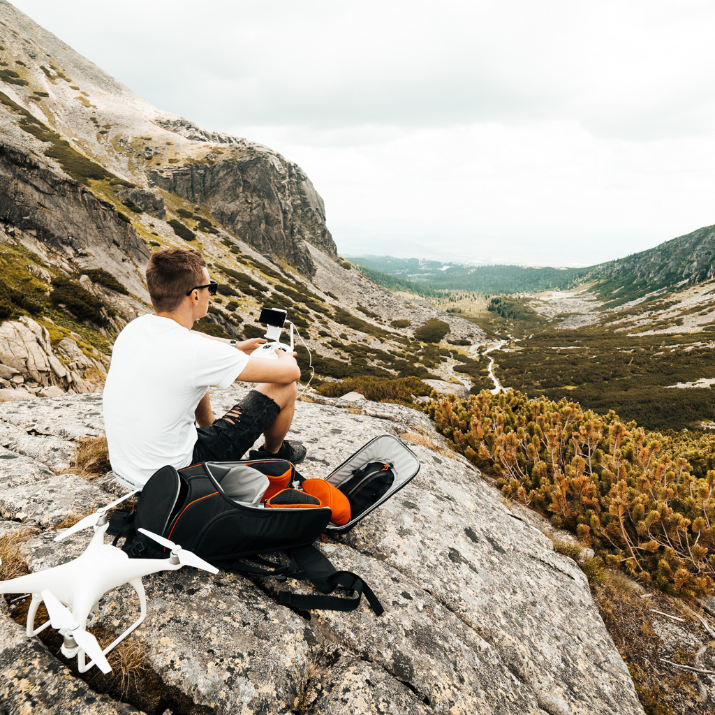 Парень с квадрокоптером сидит на камне в горах 