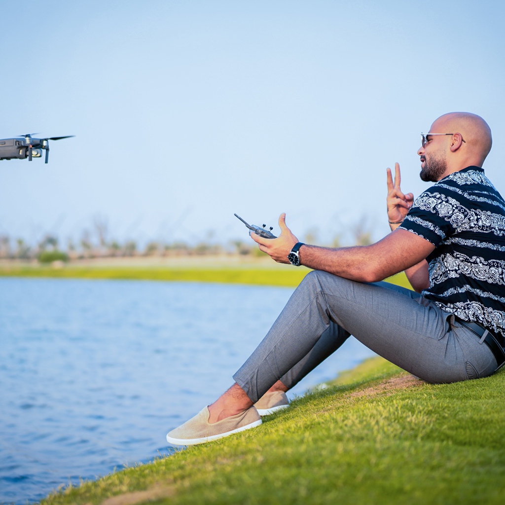Мужчина запускает квадрокоптер над озером 