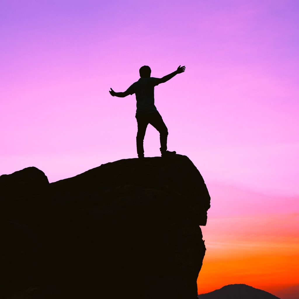 Мужчина стоит на краю утеса на закате