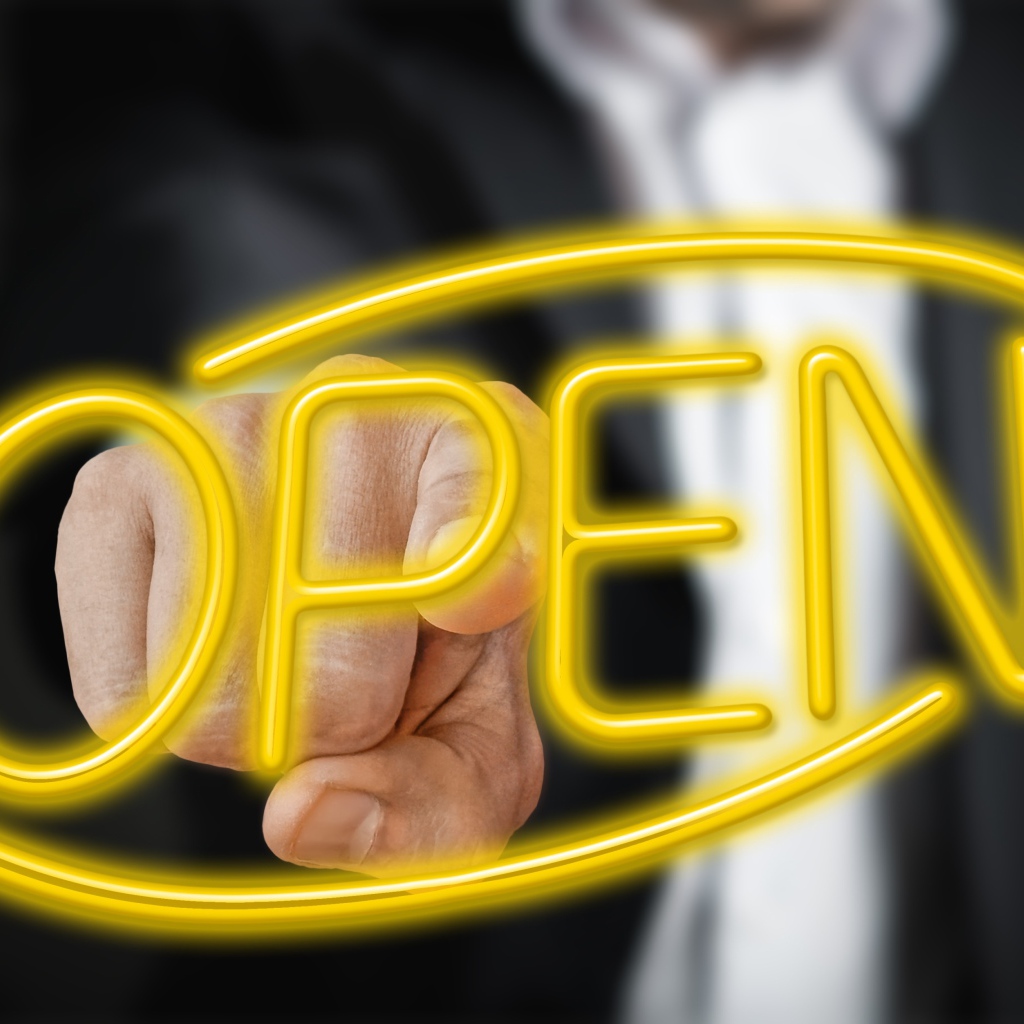 Мужчина трогает пальцем желтую  неоновую  надпись Open 