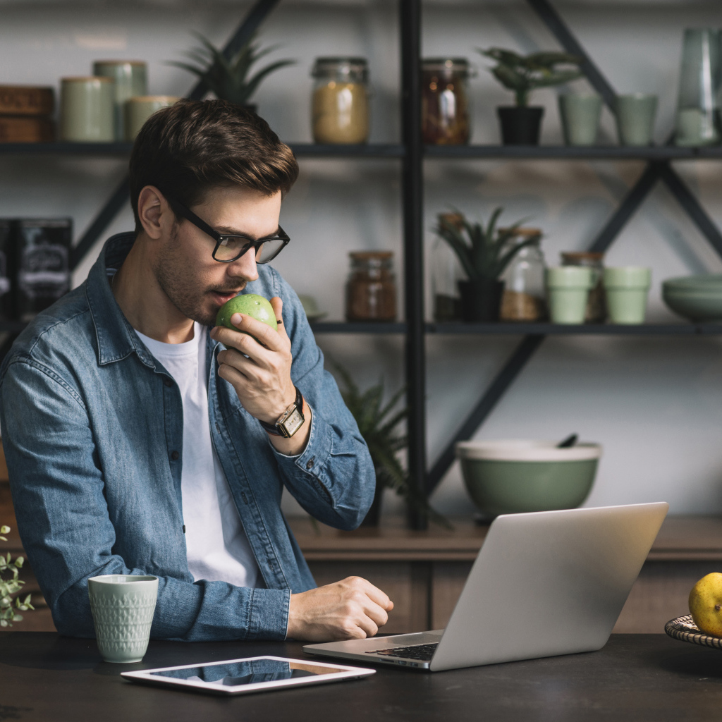 Мужчина с ноутбуком ест яблоко в кафе 