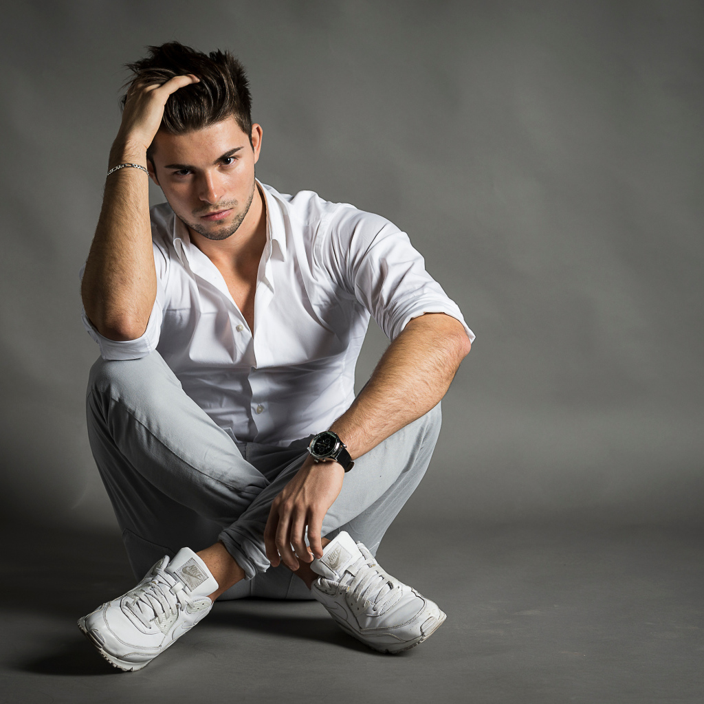 Красивый молодой человек в белой рубашке сидит у стены 