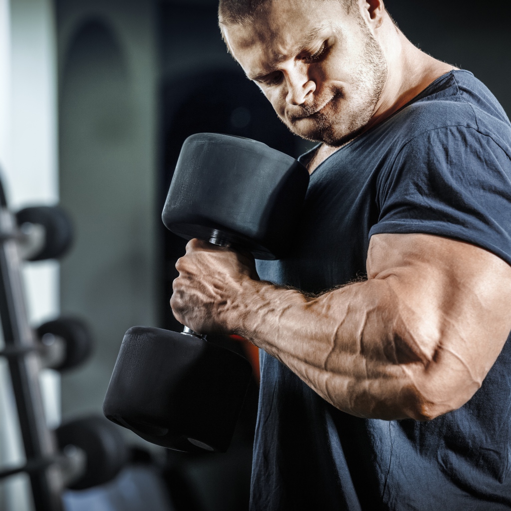 Мужчина бодибилдер в спортзале с гантелей 
