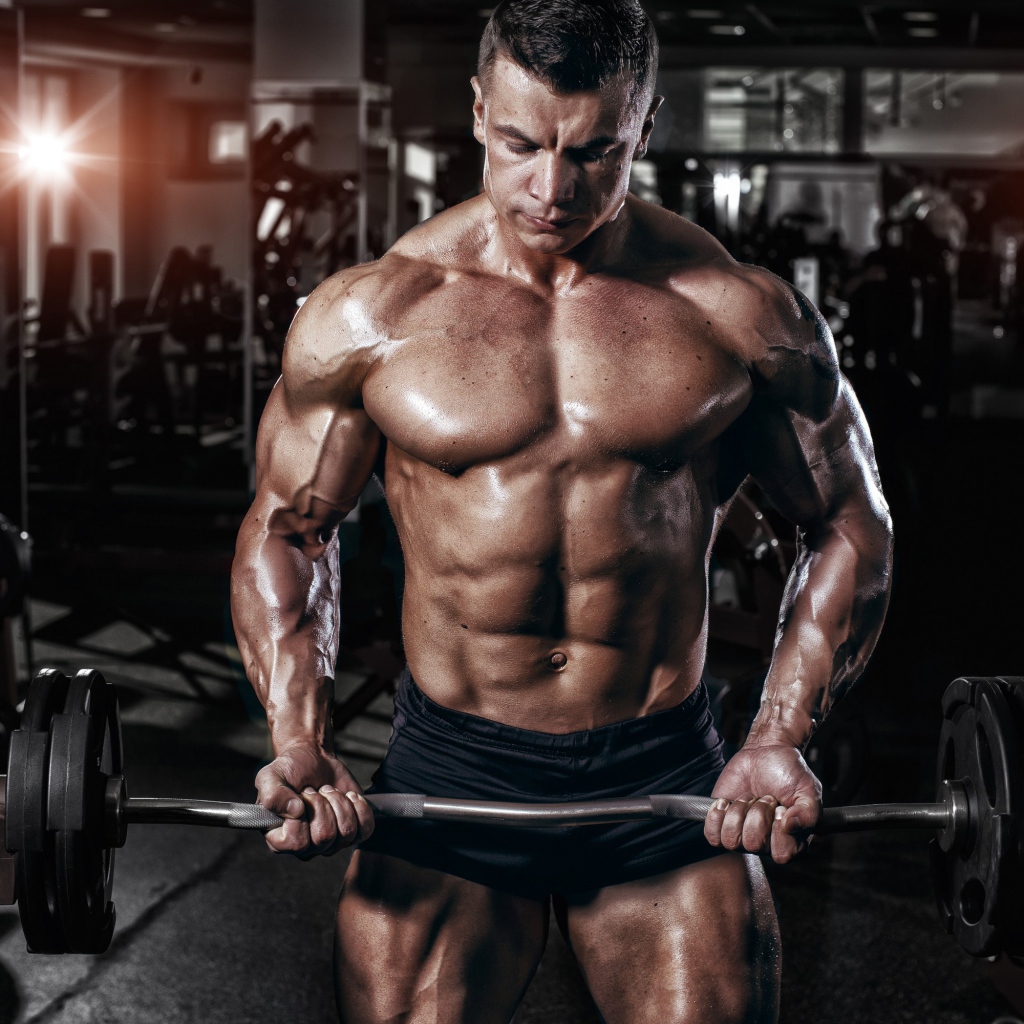 Мускулистый мужчина со штангой в руках в спортзале
