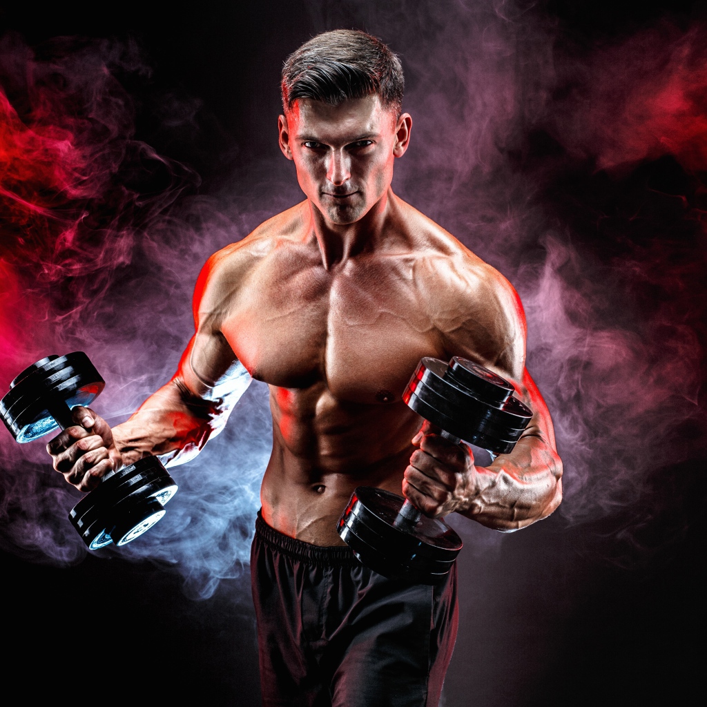 Мускулистый мужчина с гантелями в руках на черном фоне с дымом