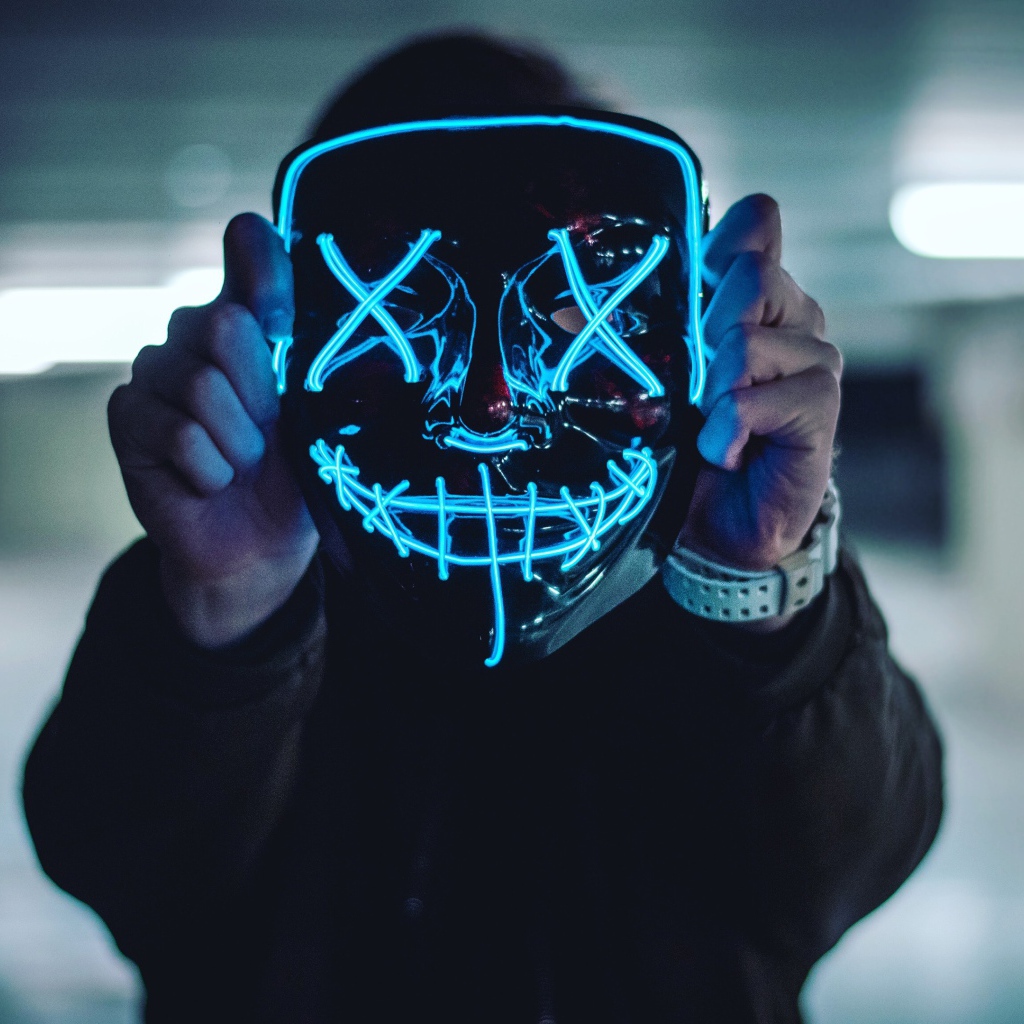 Неоновая маска анонима в руках у парня 