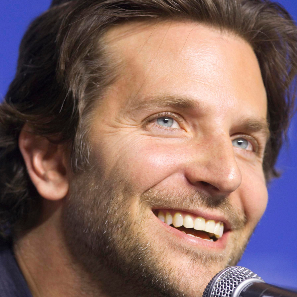 Голубоглазый актер Брэдли Купер с микрофоном на синем фоне