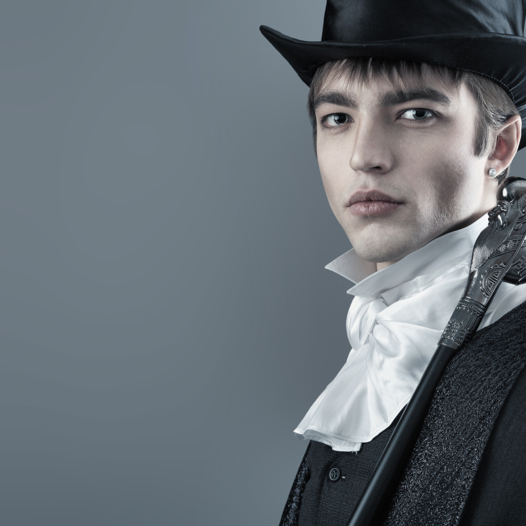 Красивый молодой человек в черном цилиндре и фраке на сером фоне