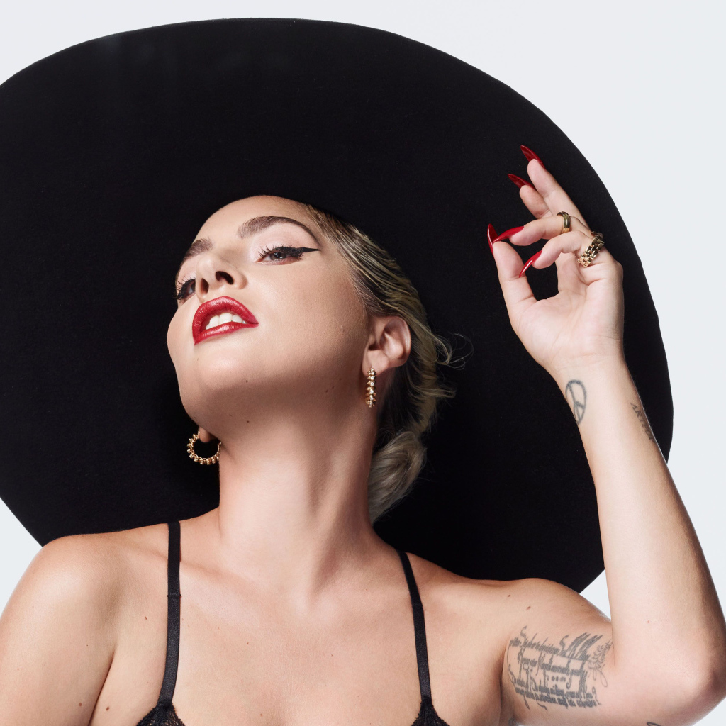 Певица Леди Гага в большой черной шляпе на белом фоне