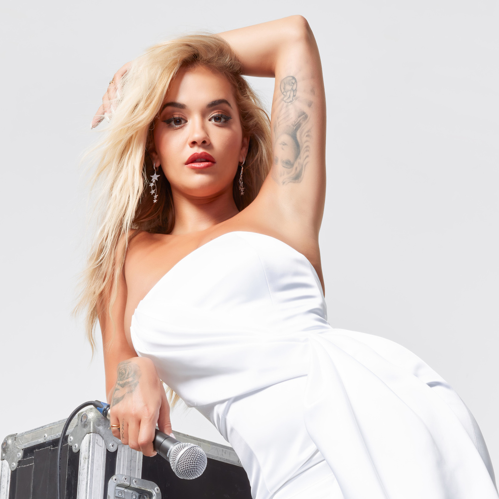 Певица Рита Ора в белом платье с микрофоном