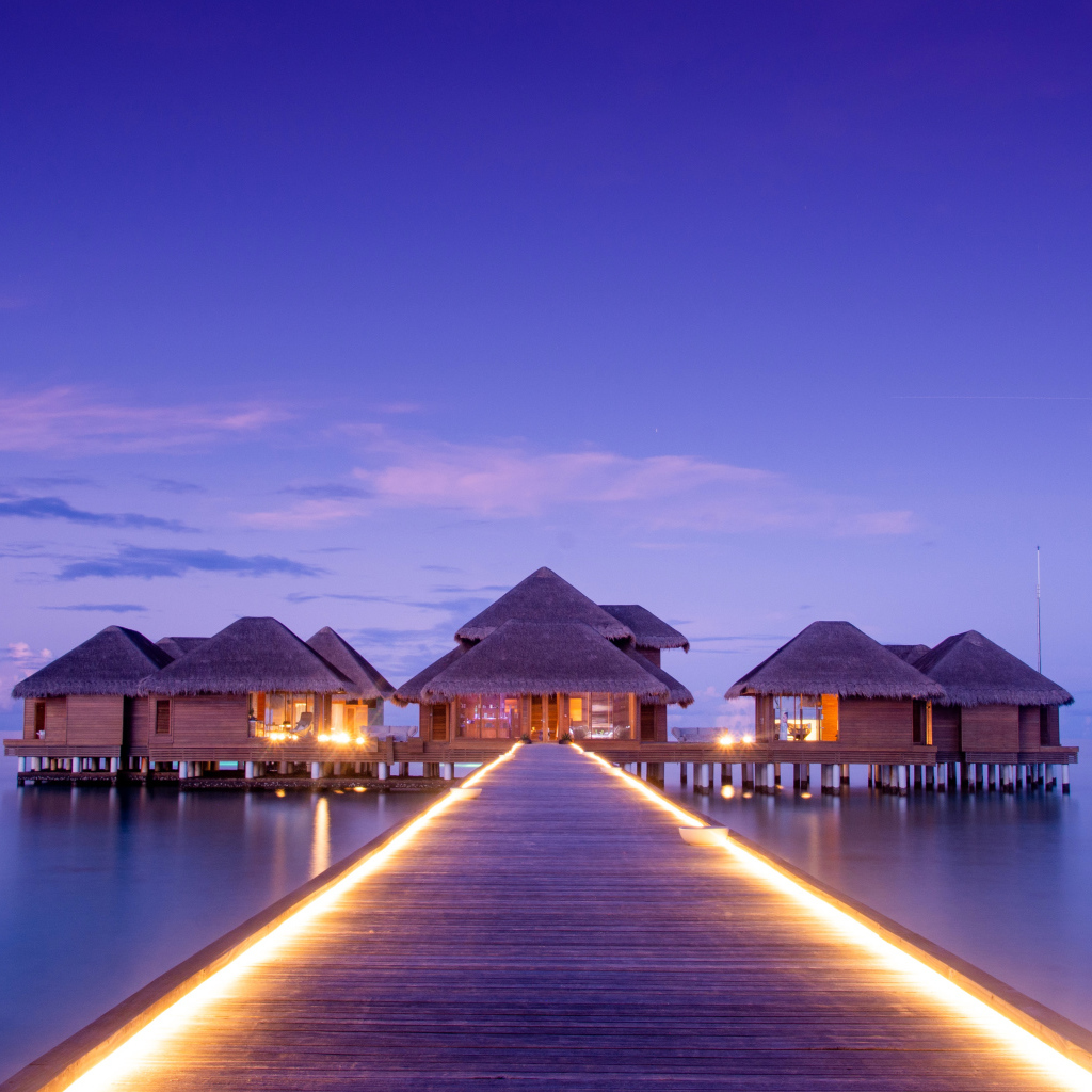 Мост с подсветкой идет к домам на сваях в океане