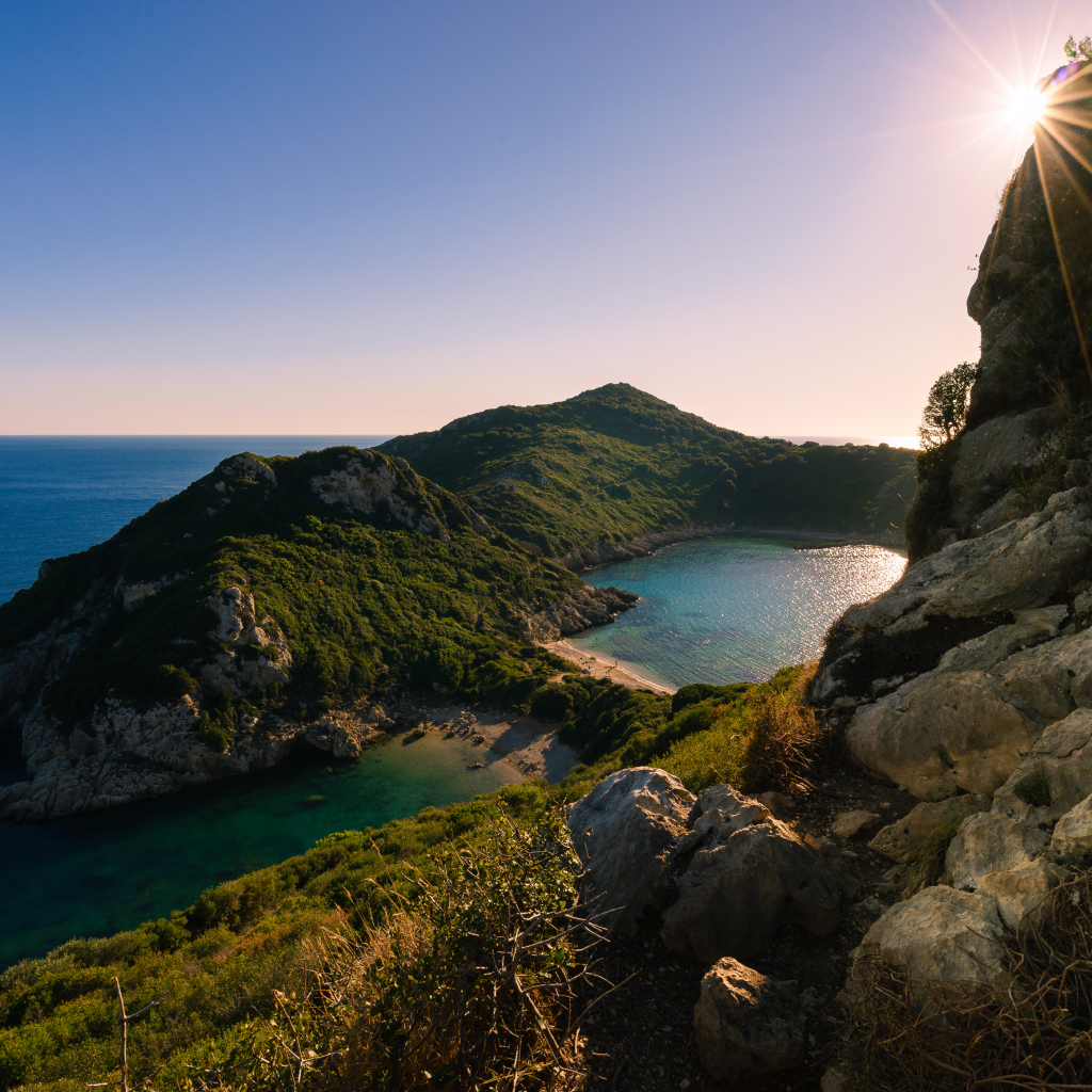 Яркое солнце за скалой у тихого моря