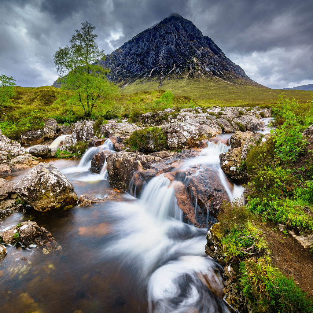 Быстрая вода в реке на фоне высокой горы под грозовым небом 