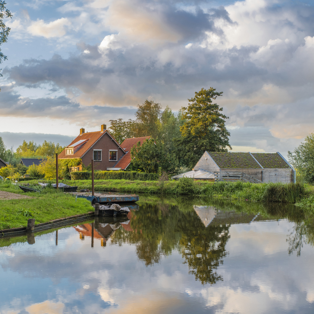 Дома отражаются в реке под небом с белыми облаками