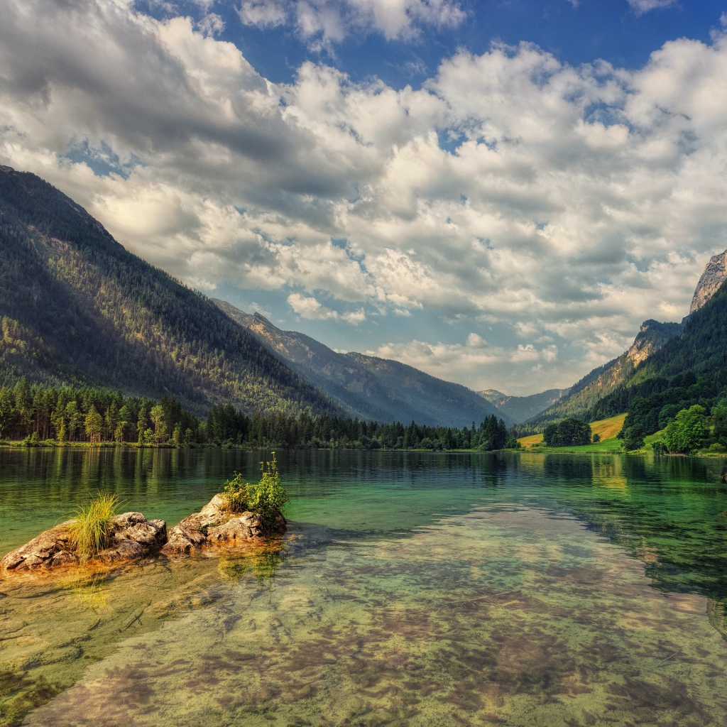 Большие камни в озере на фоне гор под небом с белыми облаками