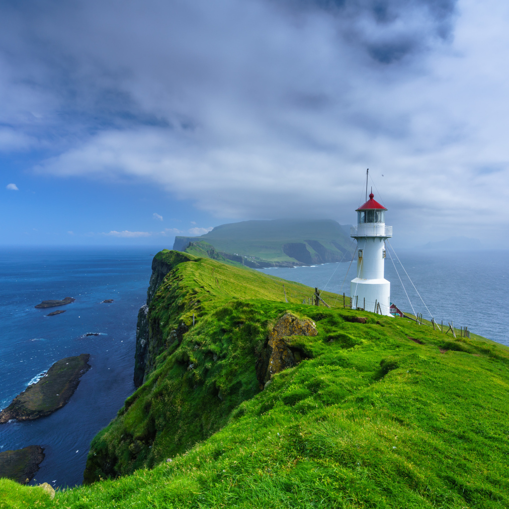 Маяк на покрытой зеленью скале под голубым небом