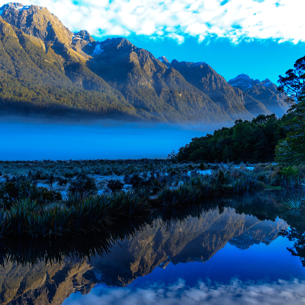 Горы и небо отражаются в голубой воде озера 