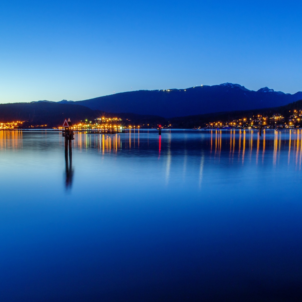 Огни ночного города отражаются в воде у гор 