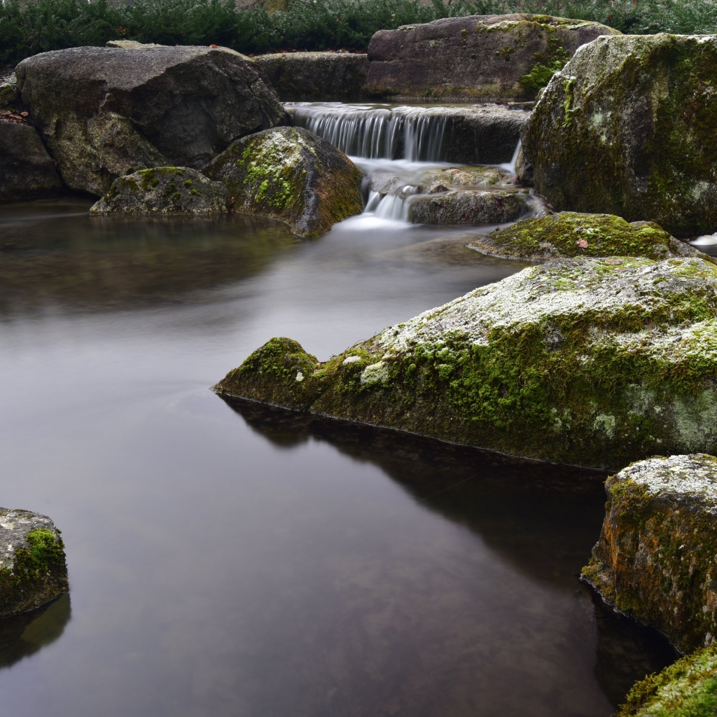 Вода стекает по камням в пруд с большими покрытыми мхом камнями