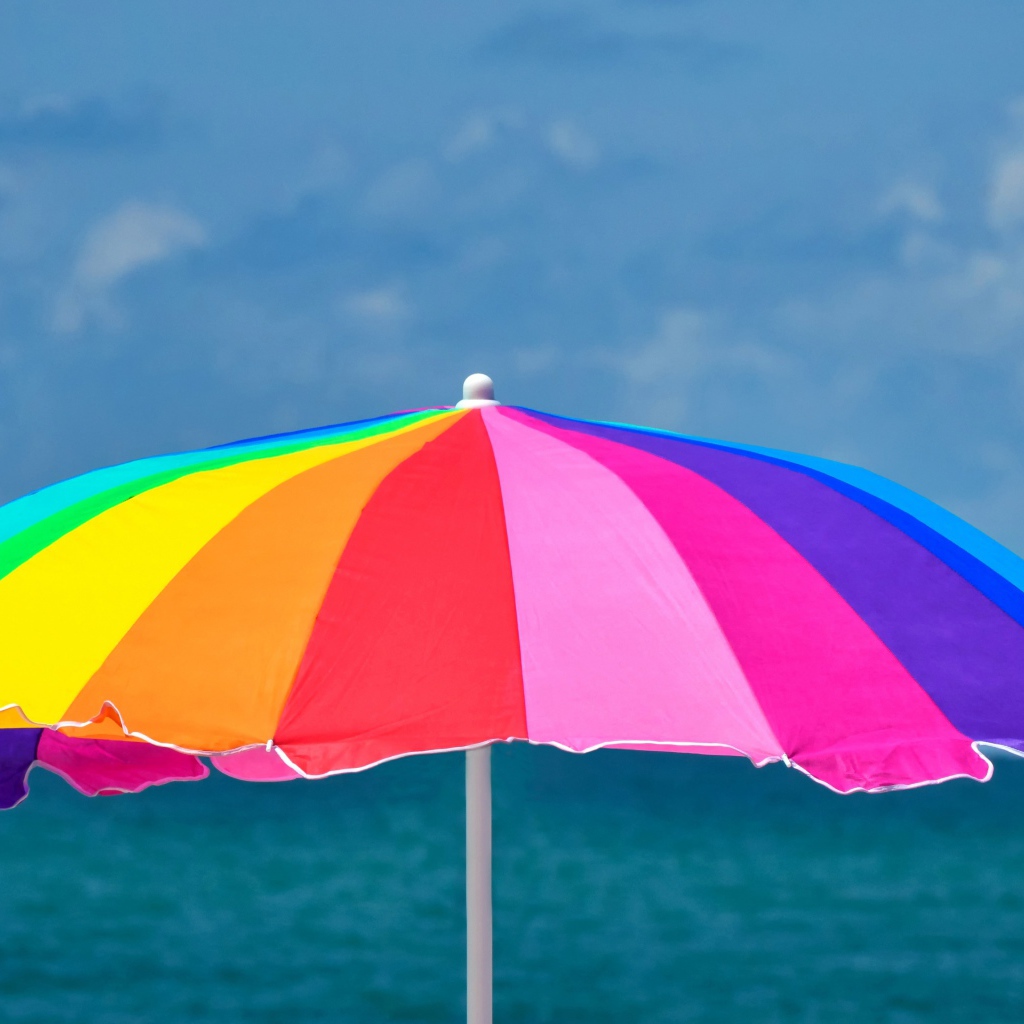 Большой разноцветный пляжный зонт на фоне моря