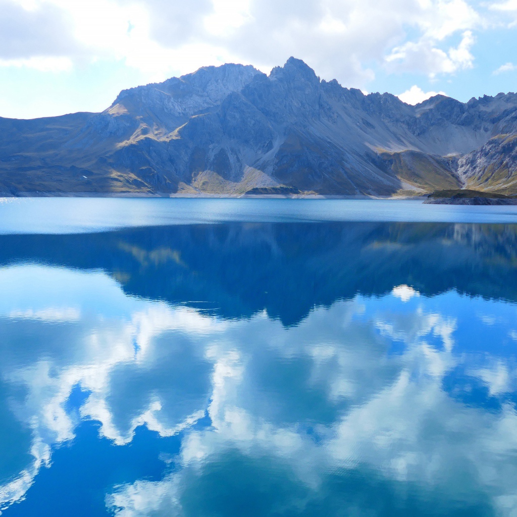 Красивые белые облака отражаются в воде озера на фоне гор 