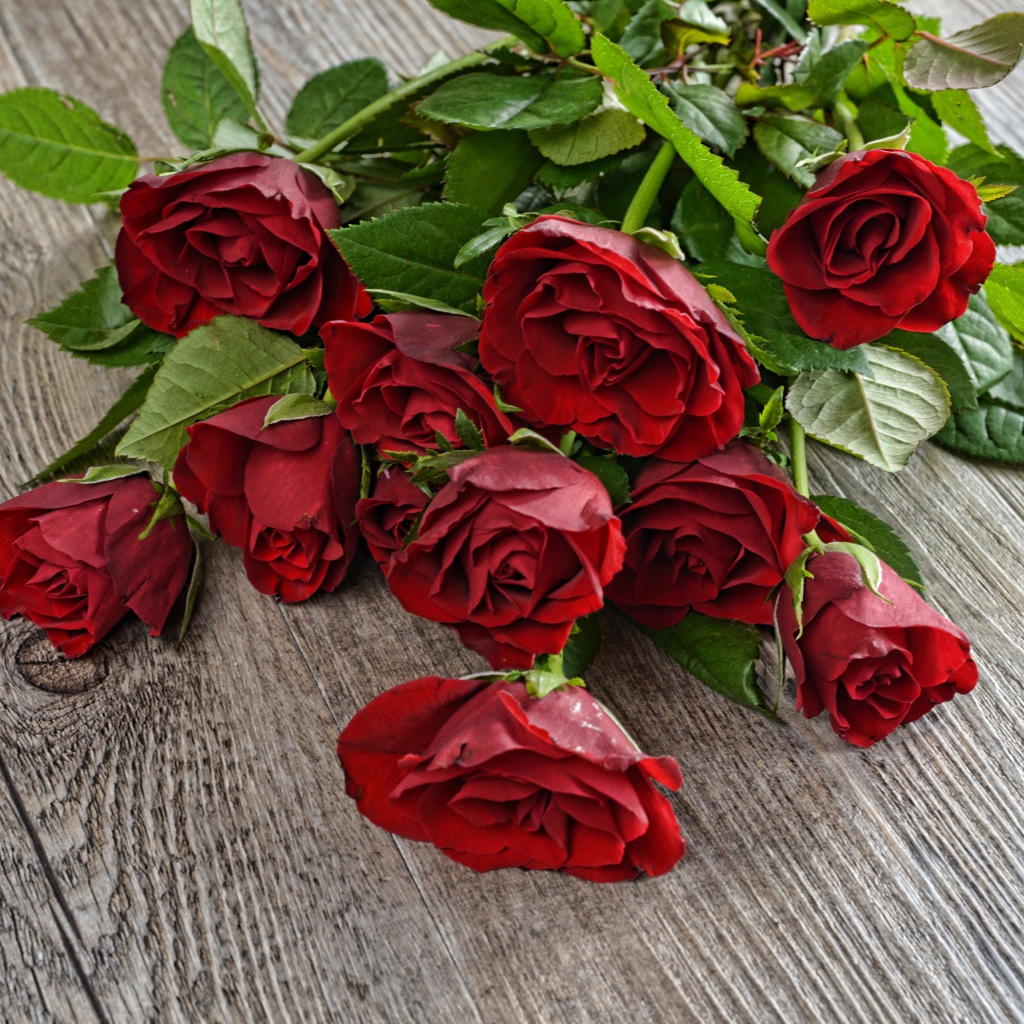 Красивый букет алых роз с зелеными листьями на деревянном столе