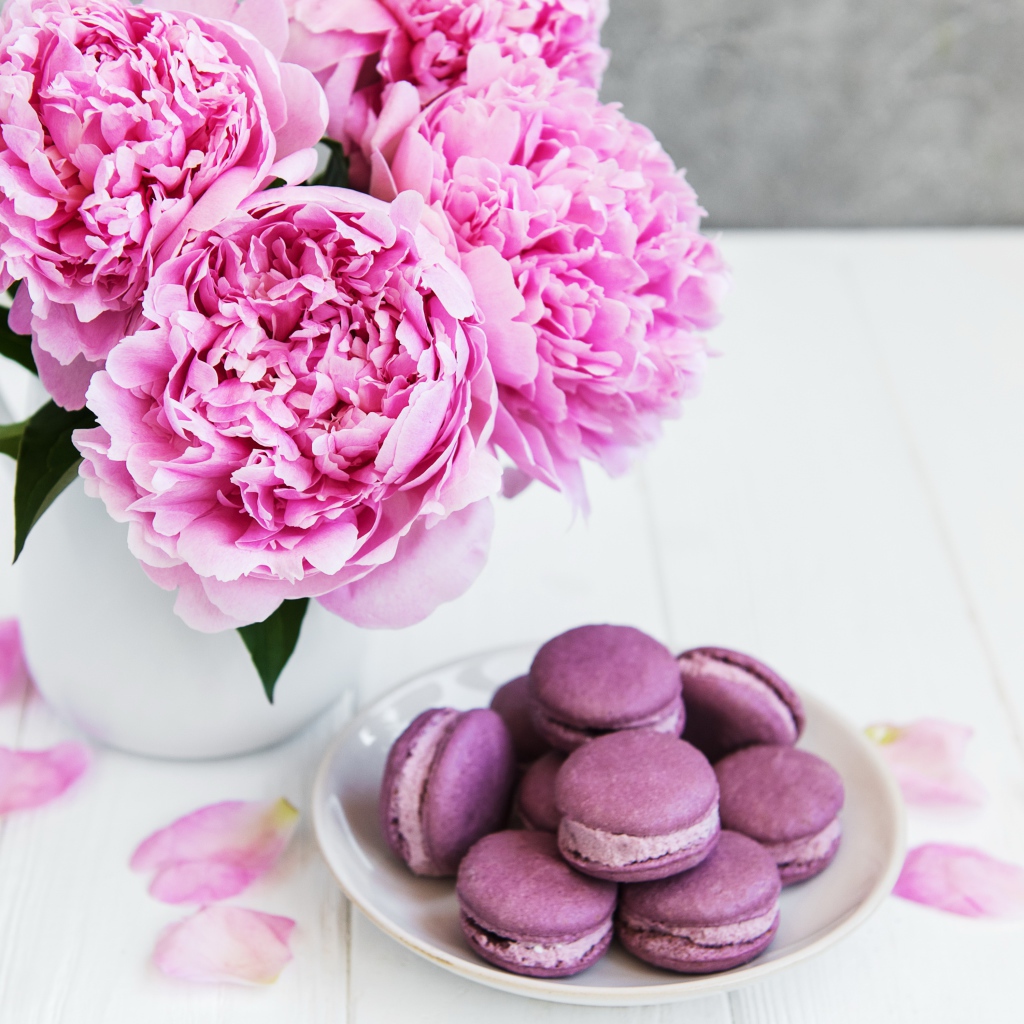 Букет розовых пионов на белом столе с десертом макарон 