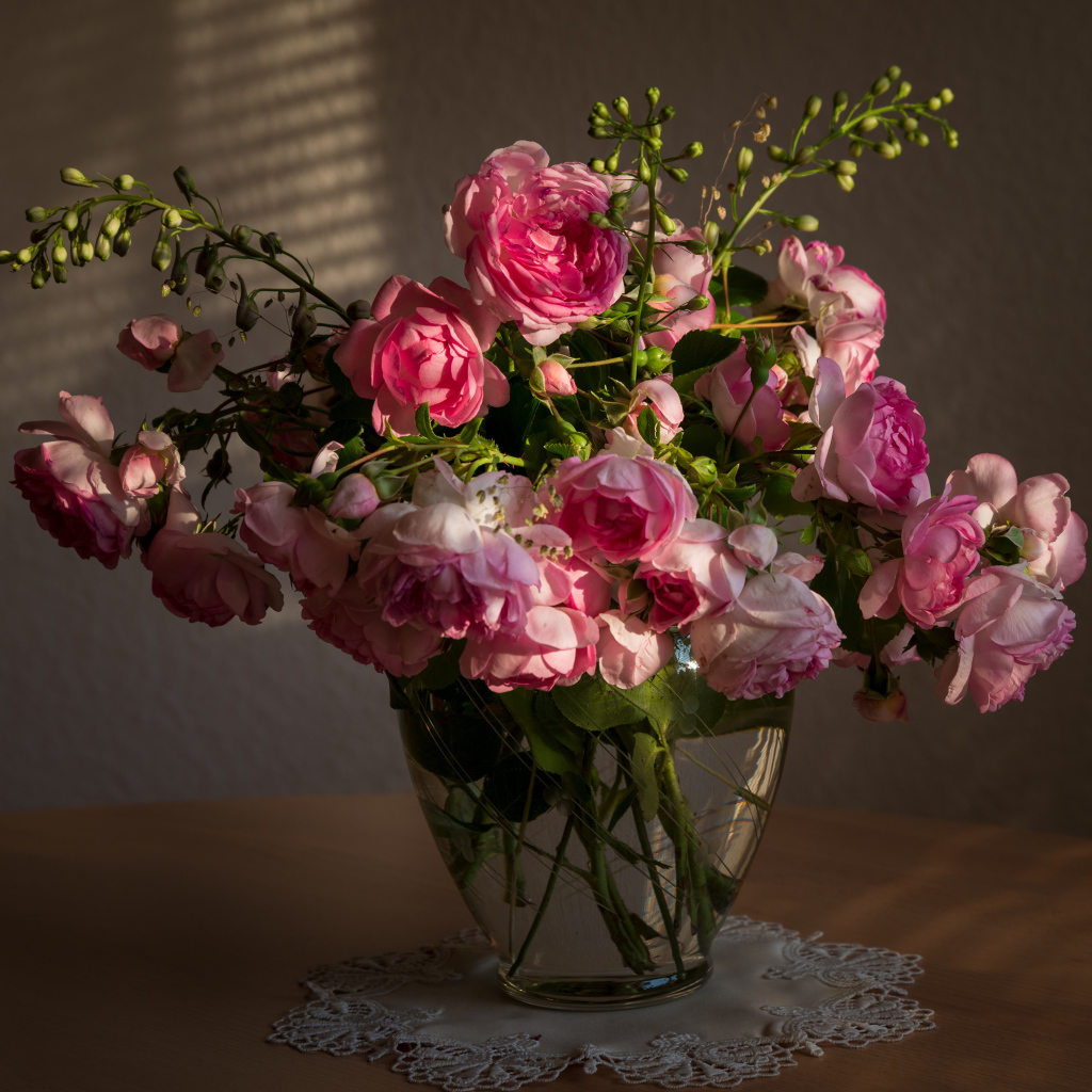 Букет розовых роз в стеклянной вазе не столе в лучах солнца 