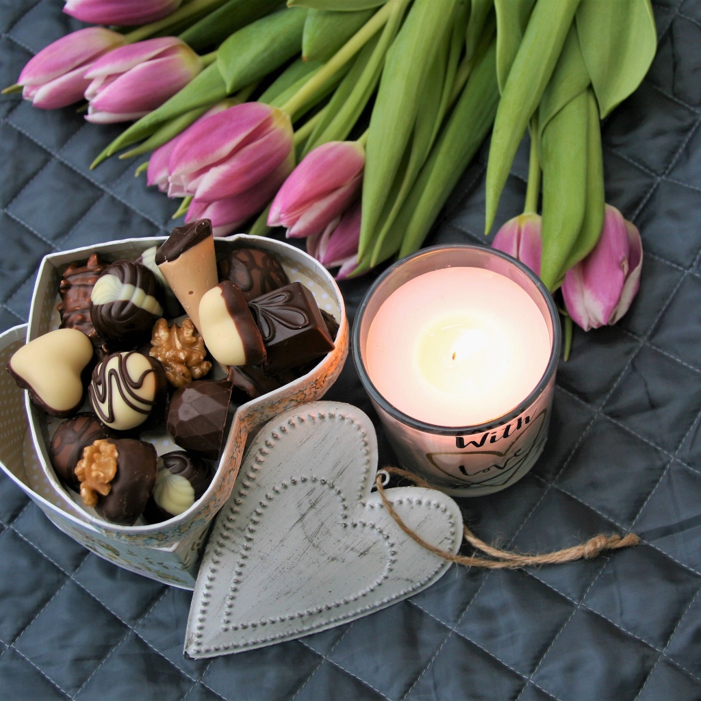 Букет розовых тюльпанов на кровати со свечой и коробкой конфет