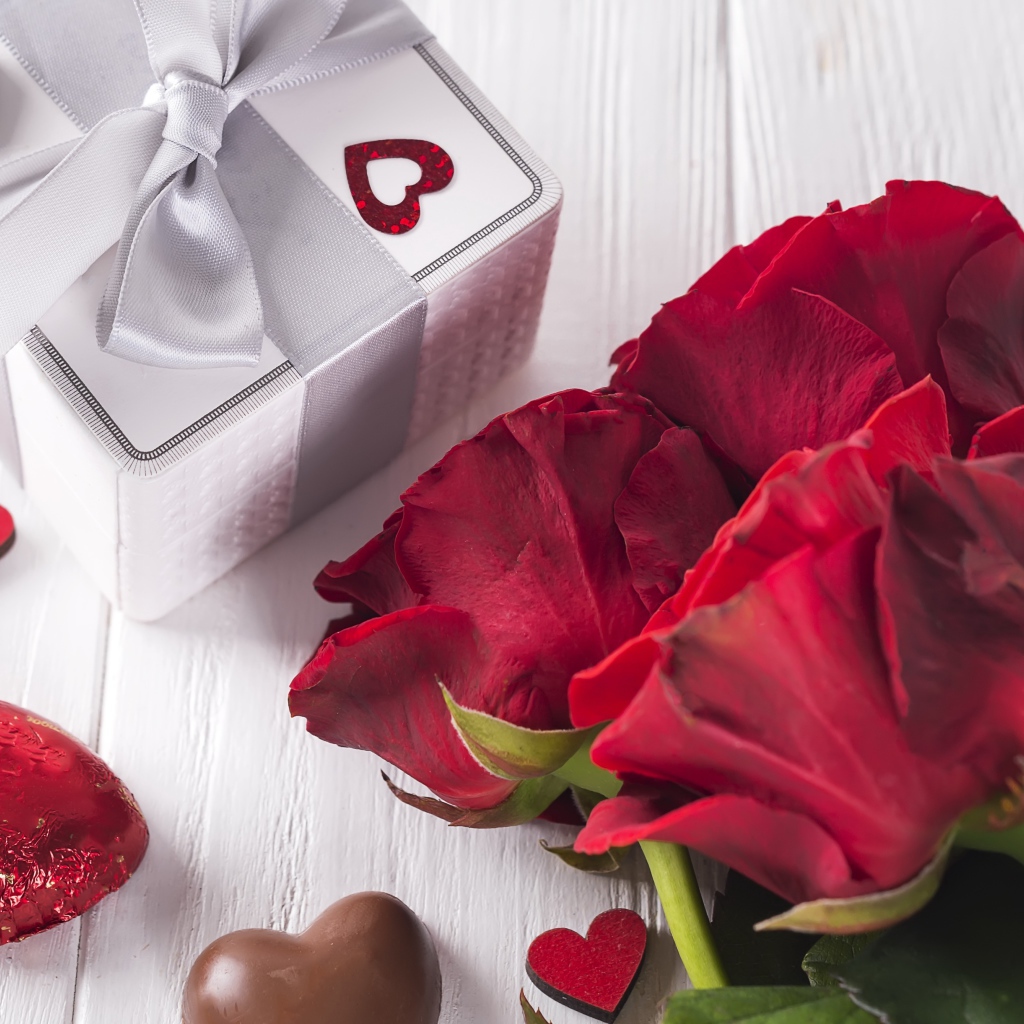 Букет красных роз на столе с конфетами и подарком