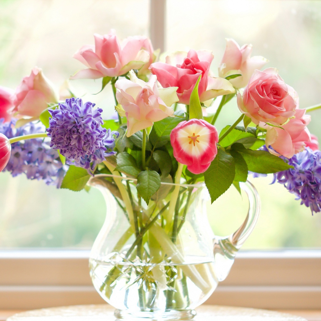 Букет роз, тюльпанов и гиацинтов в стеклянной вазе у окна