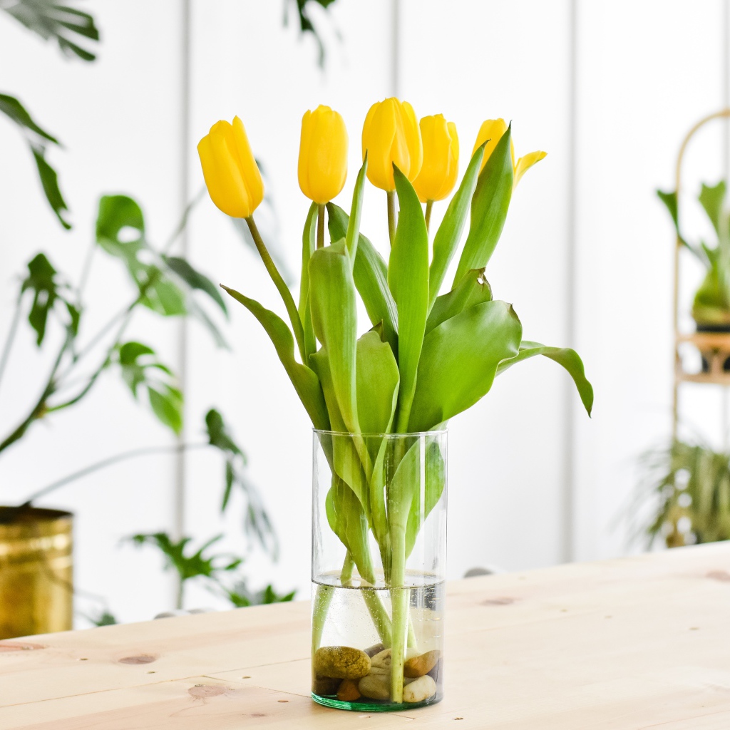 Букет желтых тюльпанов в стеклянной вазе на столе 