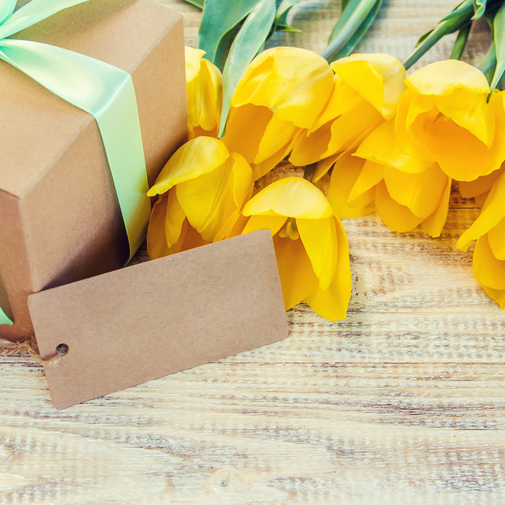 Букет желтых тюльпанов с подарком на столе 