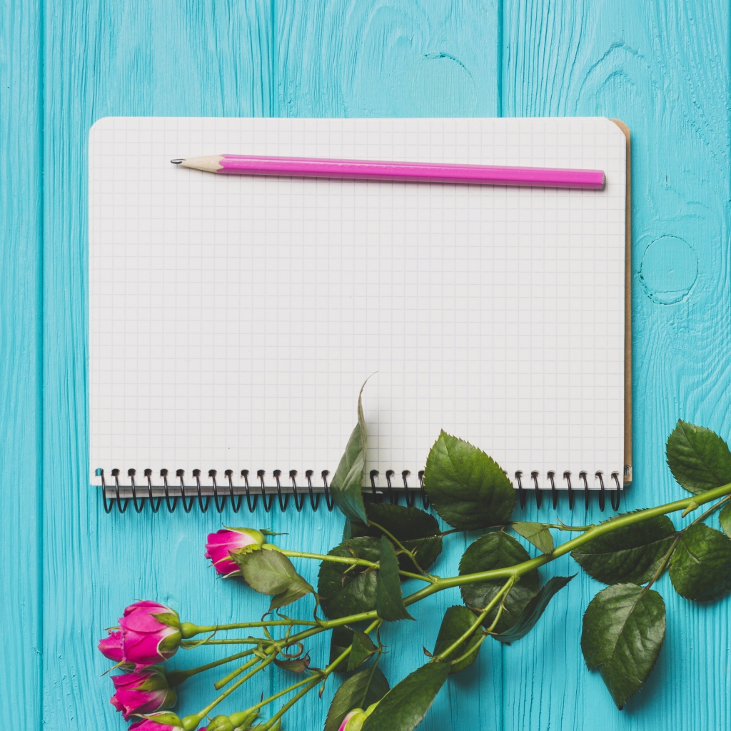 Ветка с розами на голубом фоне с блокнотом и карандашом