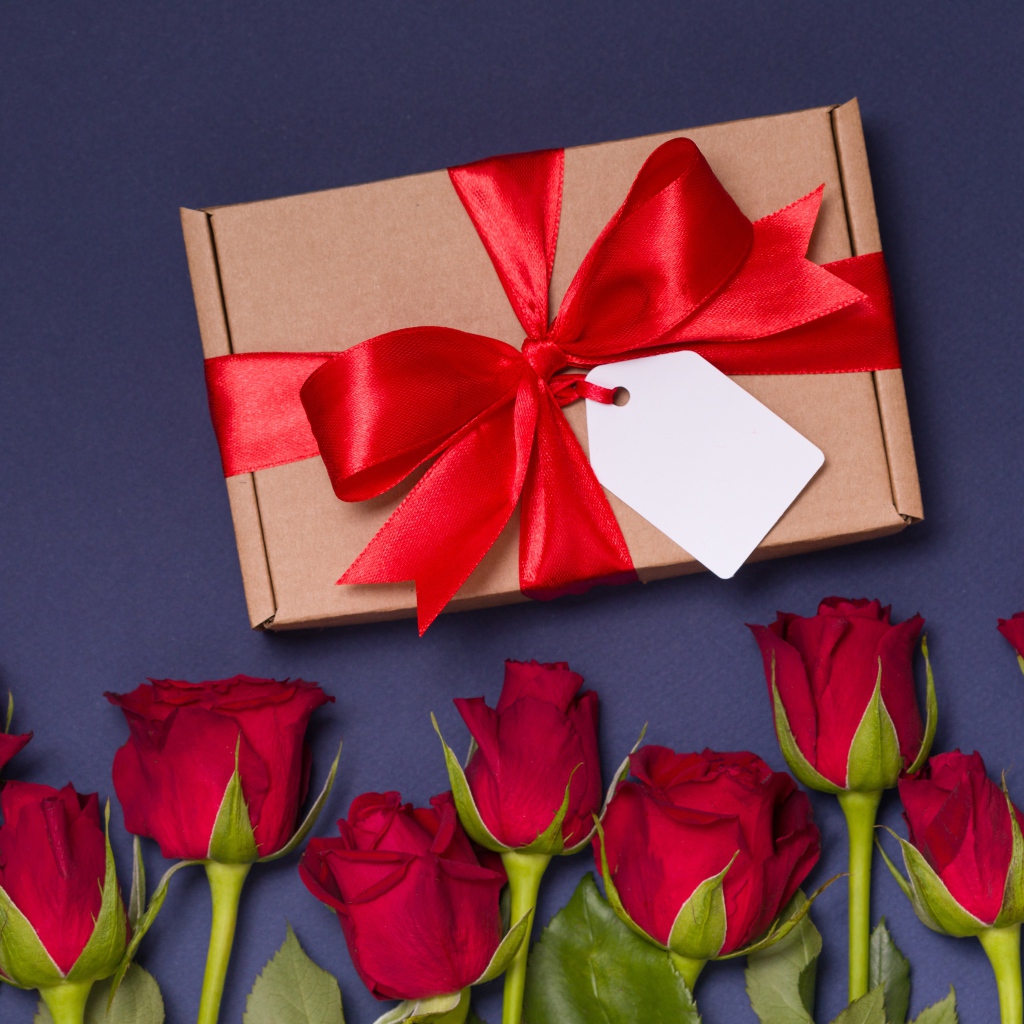 Подарок с красным бантом на столе с розами