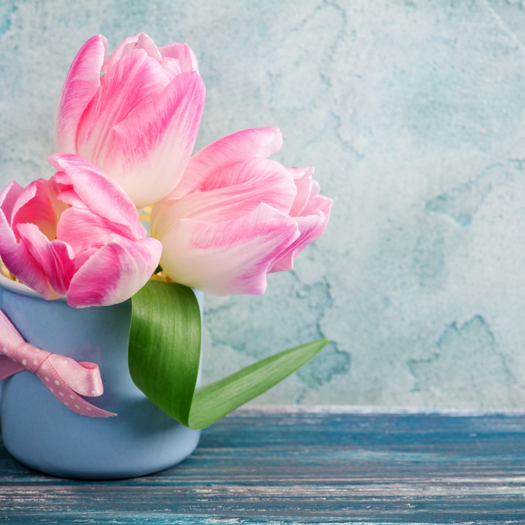 Три розовых тюльпана в чашке на столе 