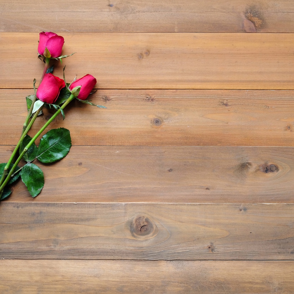 Три красные розы лежат на деревянном столе 