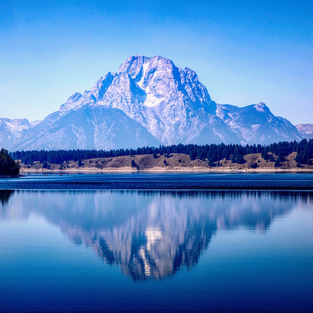 Высокие горы отражаются в озере под голубым небом