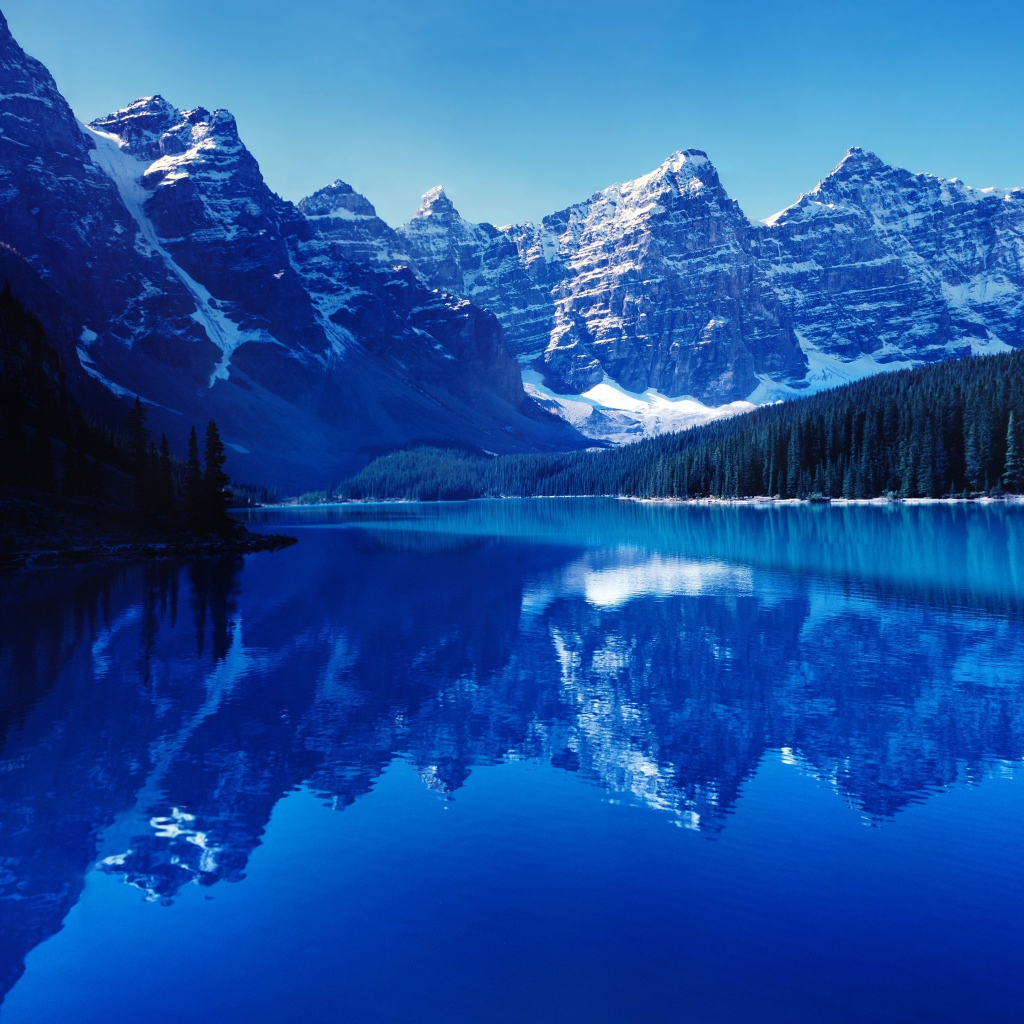 Высокие заснеженные горы отражаются в воде озера 