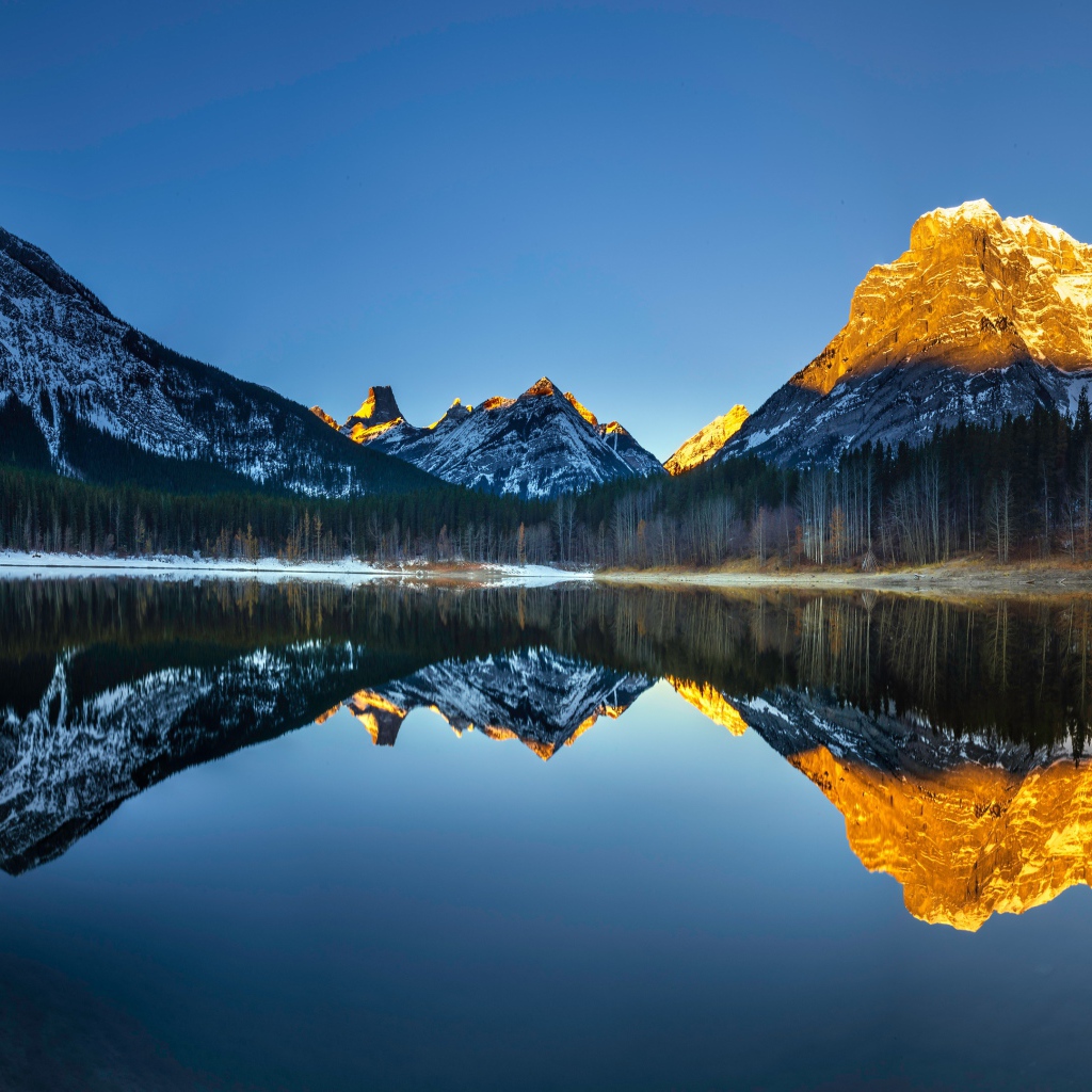 Вершины гор в лучах солнца отражаются в озере