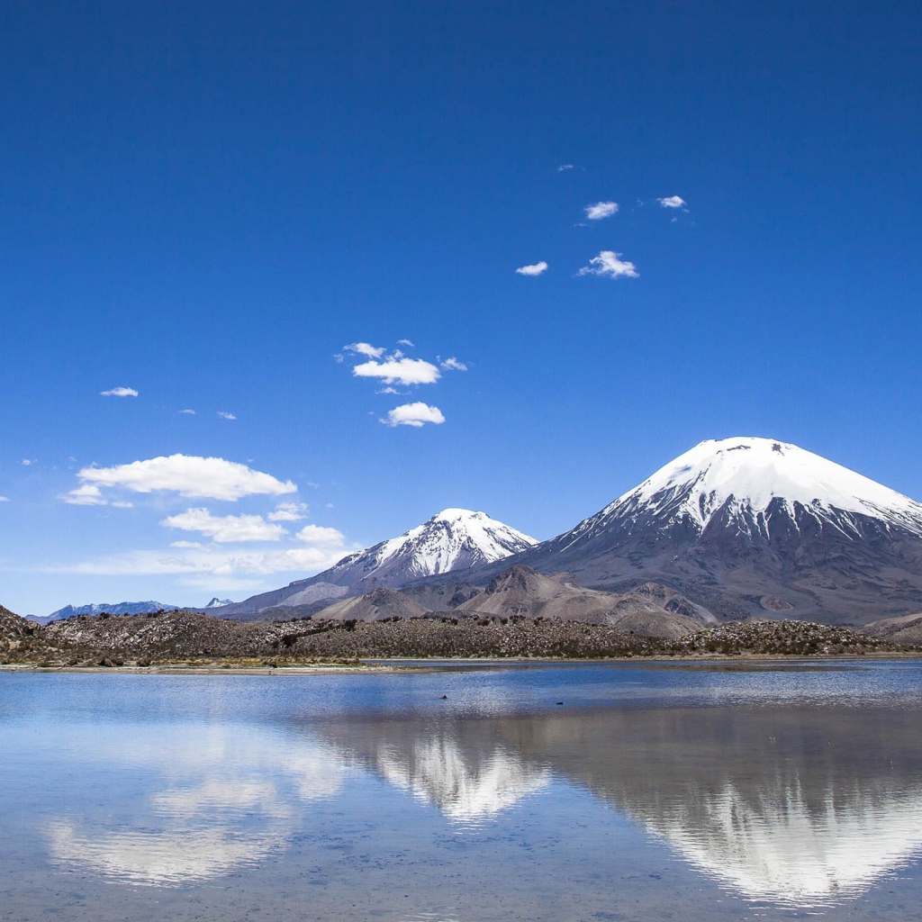 Заснеженные вершины гор под голубым небом отражаются в воде 