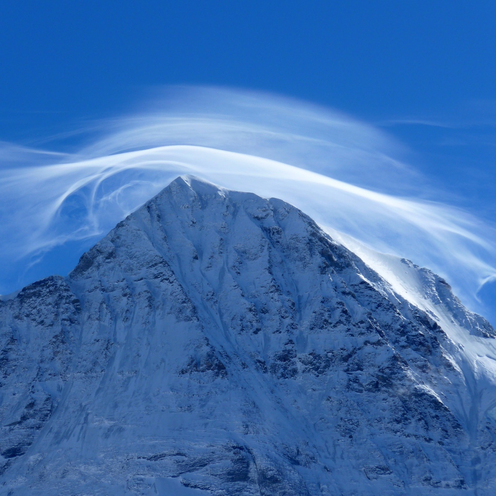 Белое облако в голубом небе над заснеженной горной вершиной