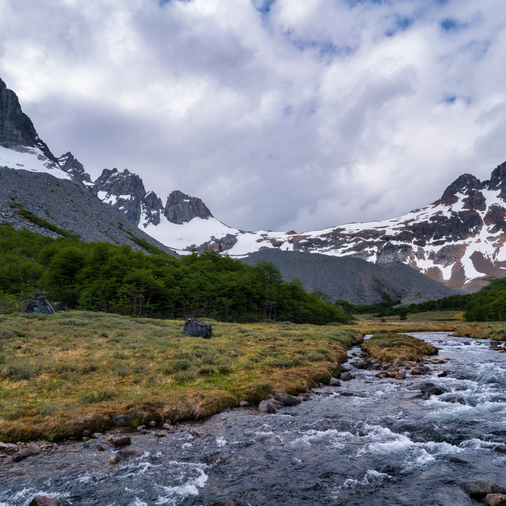 Быстрая река у заснеженных гор под густыми белыми облаками