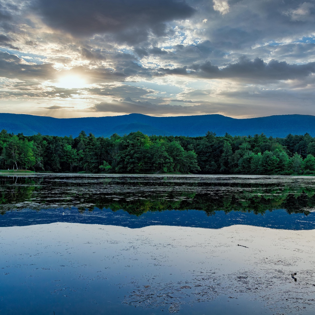 Солнце пробивается сквозь облака в небе над озером