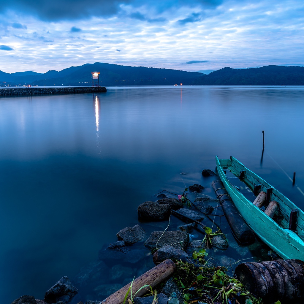 Деревянная лодка на берегу тихого озера в сумерках 
