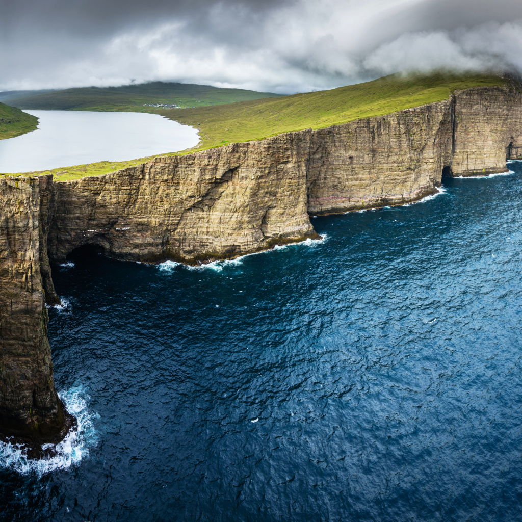 Океан омывает зеленый утес под пасмурным небом