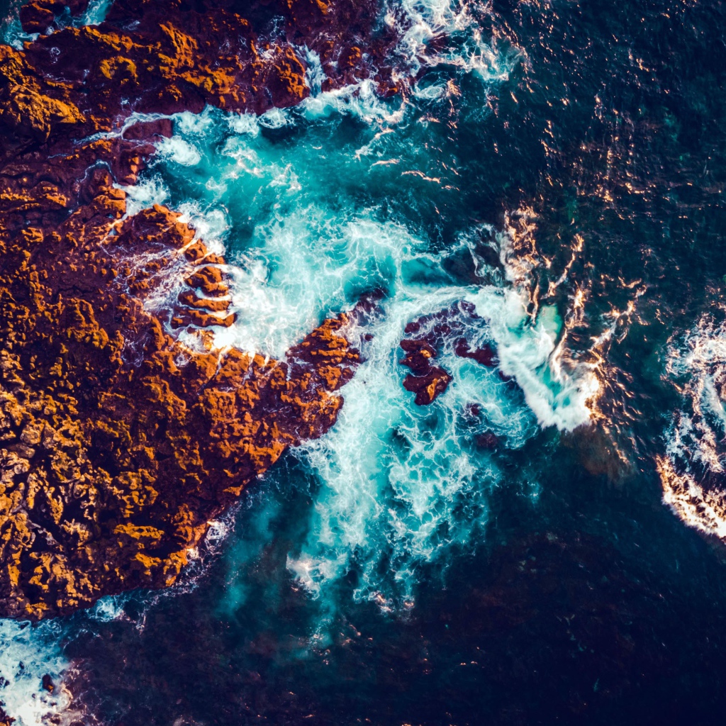 Белые морские волны бьются об камни, вид сверху