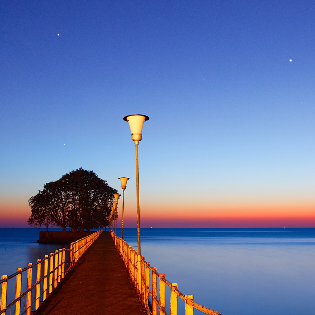 Мост в фонарями в море на закате 