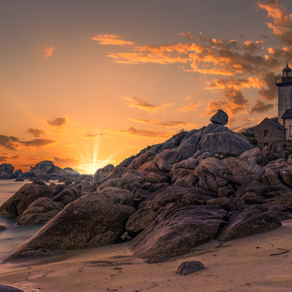 Маяк на берегу каменного берега на закате 