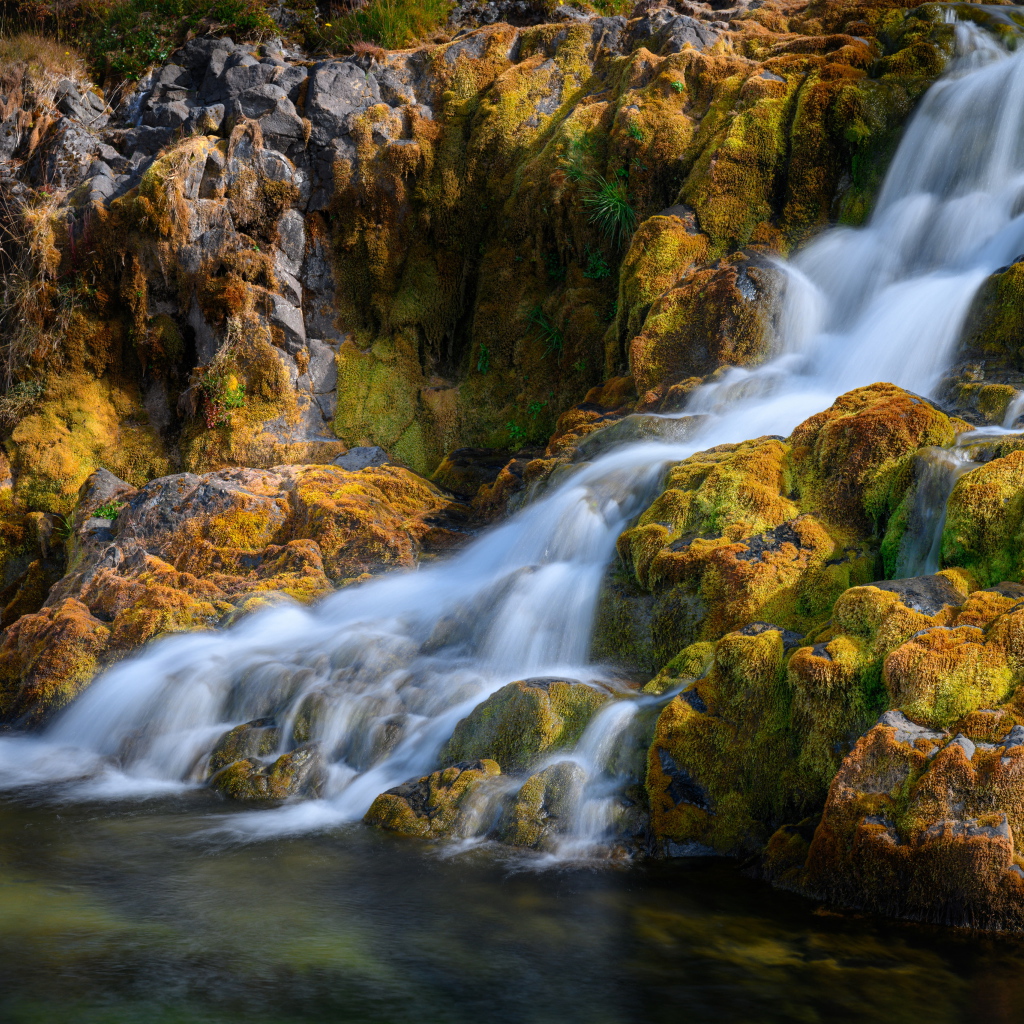 Быстрая вода водопада стекает по покрытым мхом камням, Исландия 